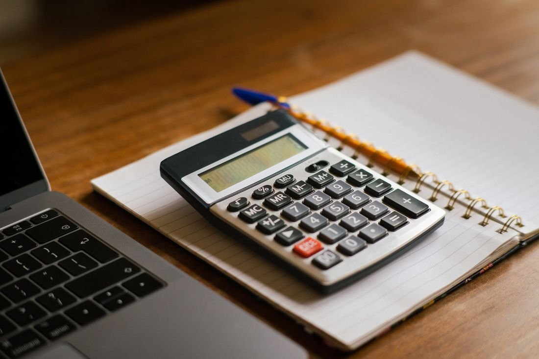 Calculator and notebook beside a laptop on a desk