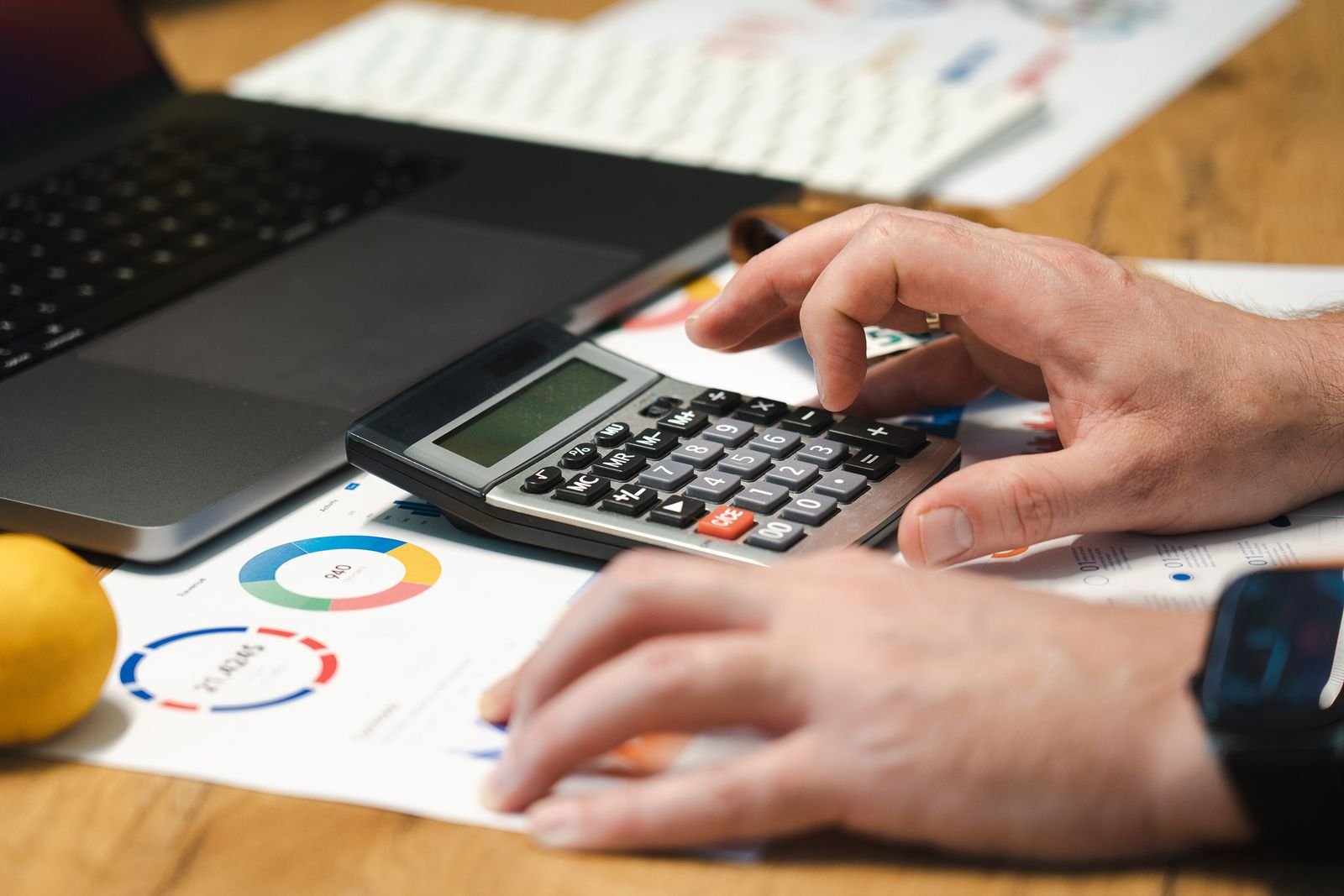 Financial analyst using a calculator beside a laptop and charts