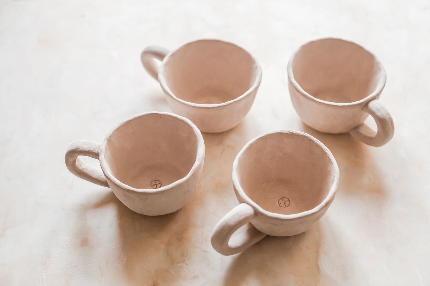 Four hand-shaped pale clay cups seen from above