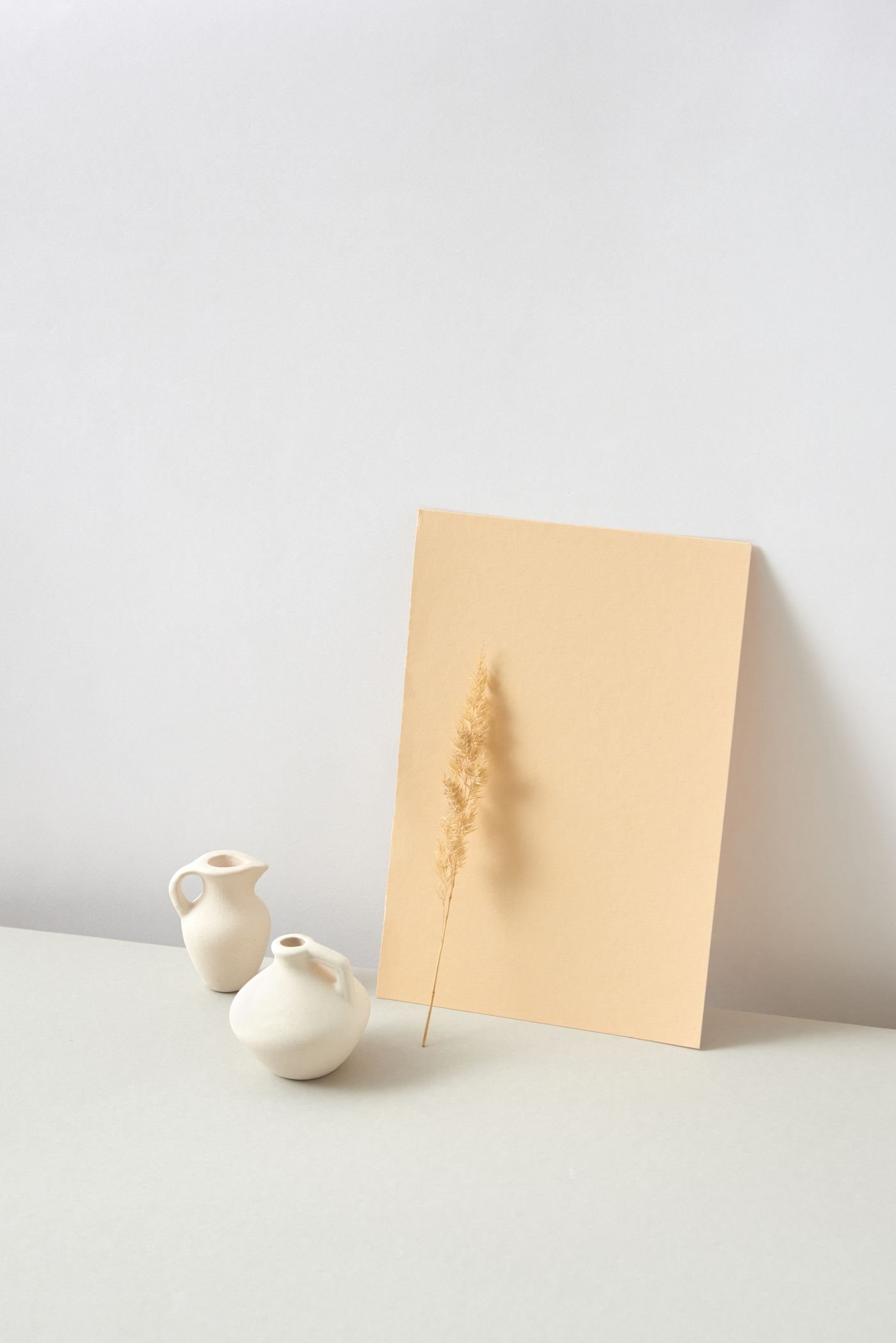 White ceramic vessels beside a dried stem and pale artwork