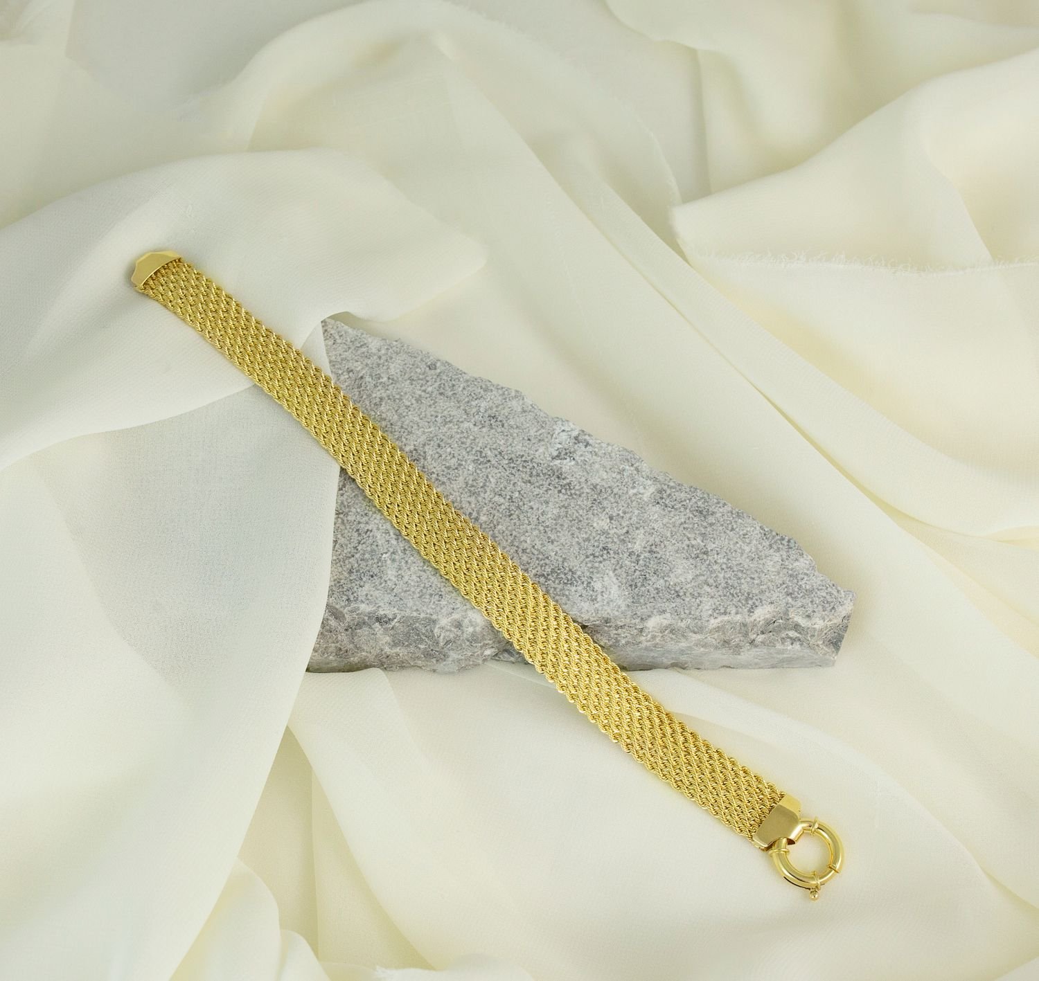 Gold chain bracelet arranged across pale fabric and stone