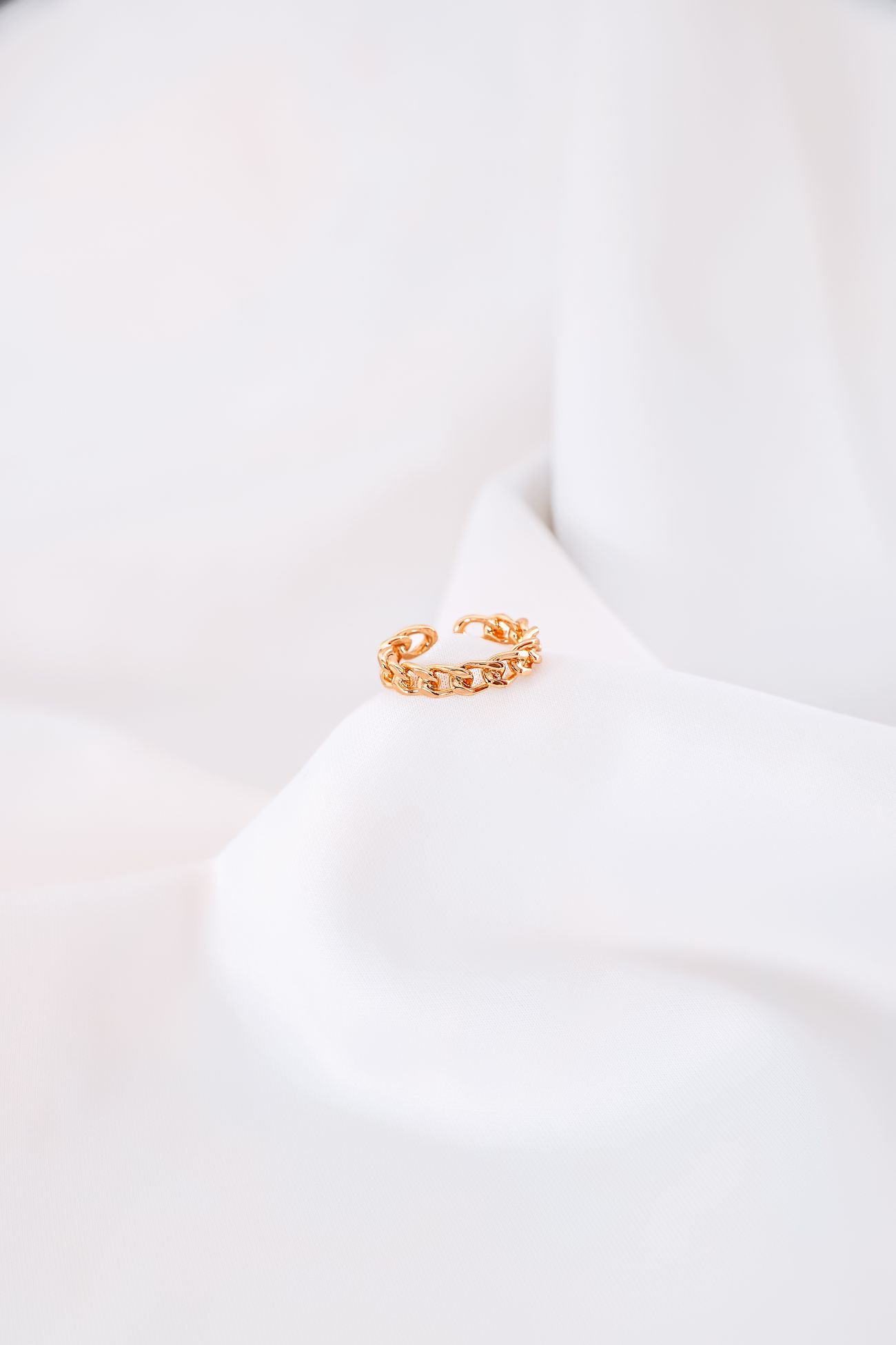 Delicate sculptural gold ring arranged on white fabric