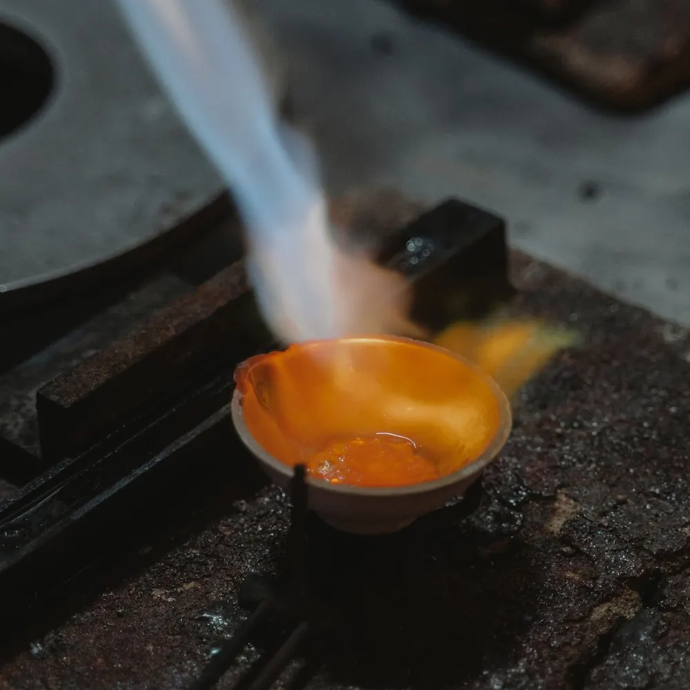 Recycled gold melting to a glowing pool in a crucible under a torch flame