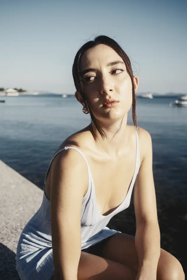 Woman in a white slip dress sitting on a harbour wall in low sun