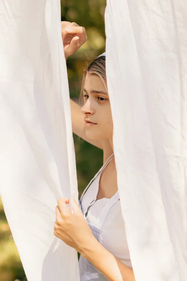 Young woman looking out between white sheets on a washing line